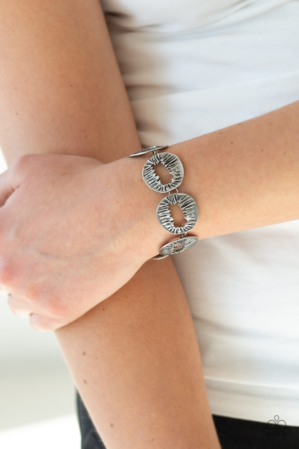 Featuring asymmetrical cutout centers, textured silver discs connect across the wrist for an abstract look.