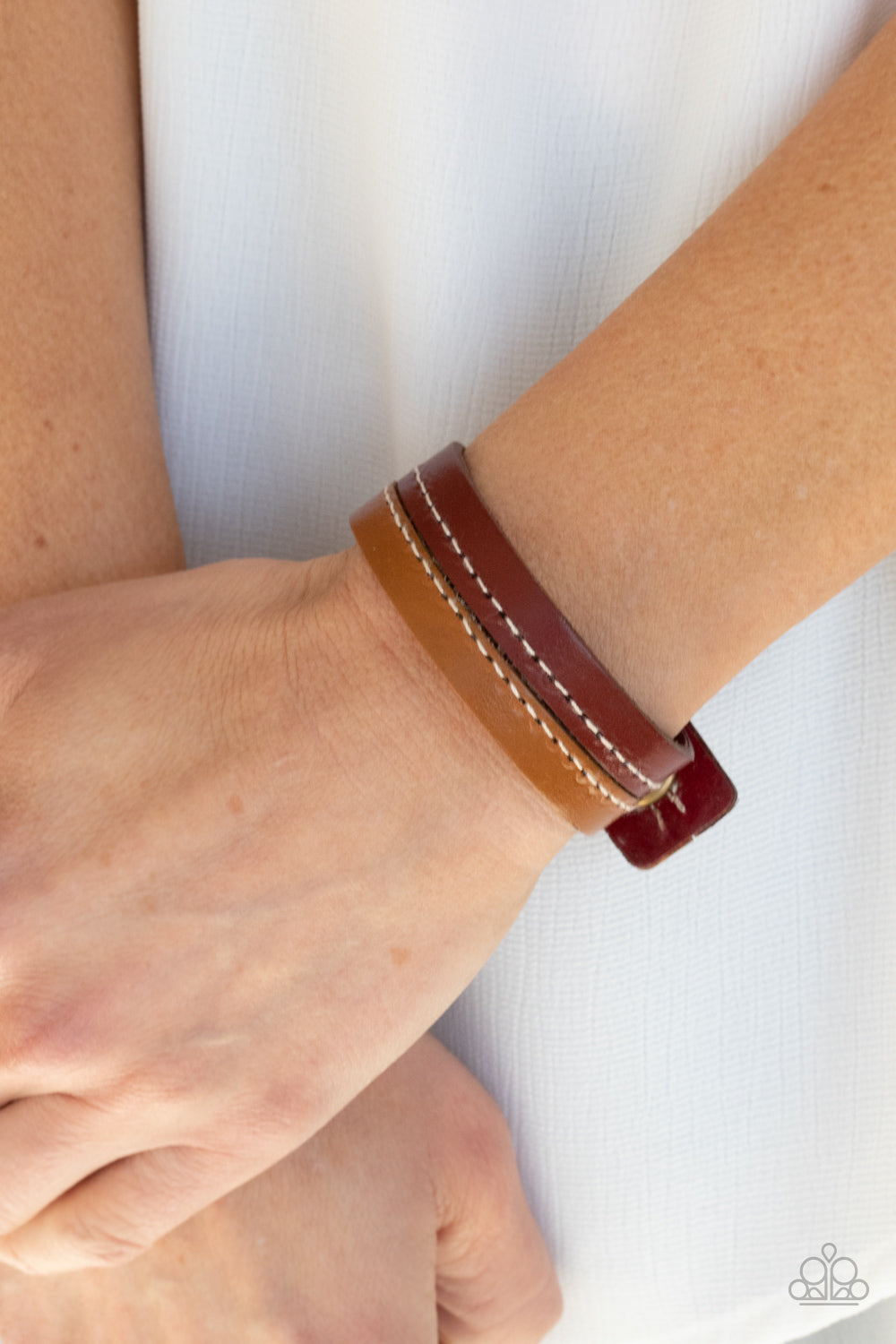 Strands of tan and red leather are stitched together, creating a rugged display around the wrist