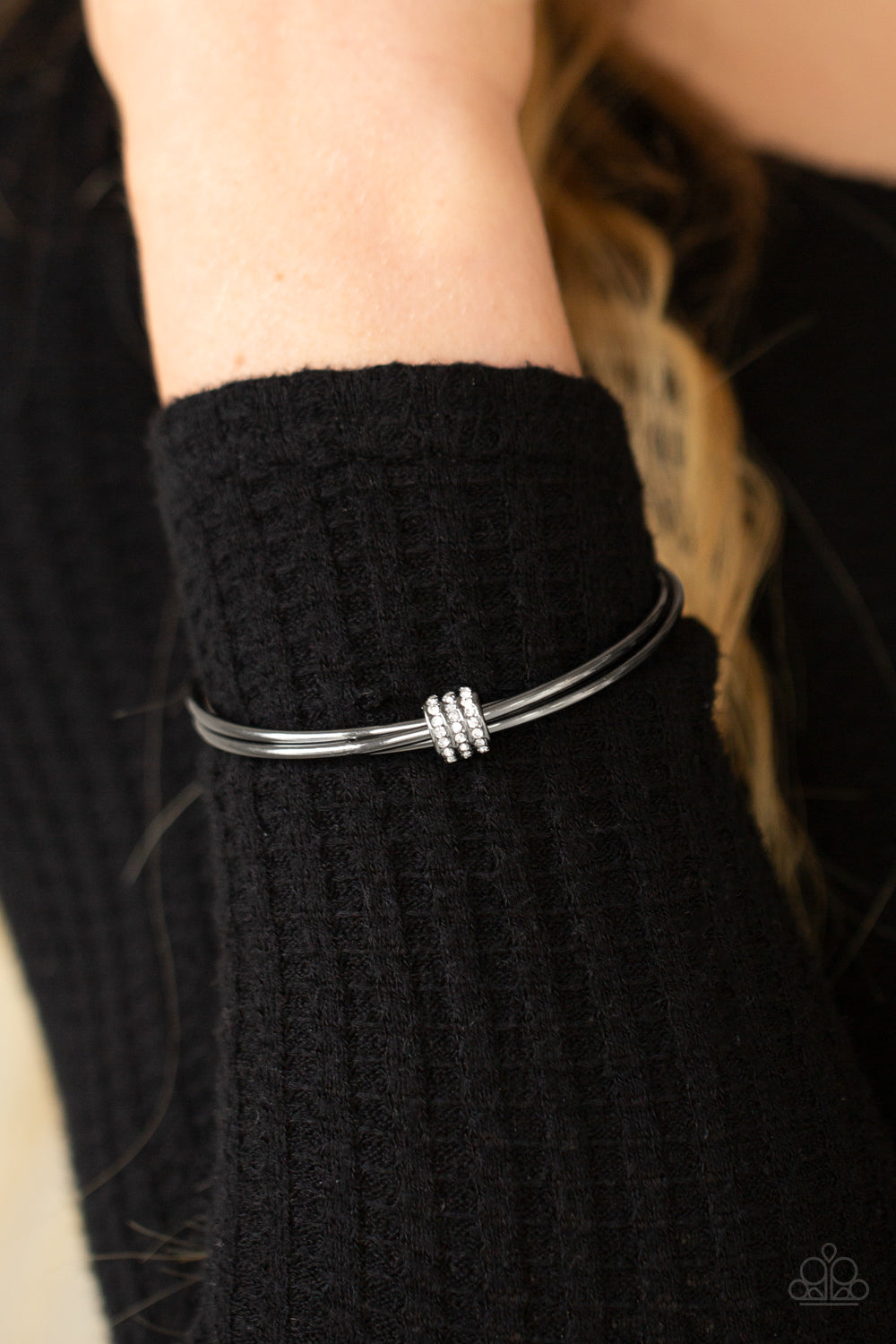 A white rhinestone encrusted fitting glides along a trio of gunmetal bangles, creating a solitaire bracelet around the wrist.