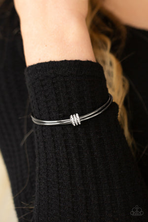 A white rhinestone encrusted fitting glides along a trio of gunmetal bangles, creating a solitaire bracelet around the wrist.