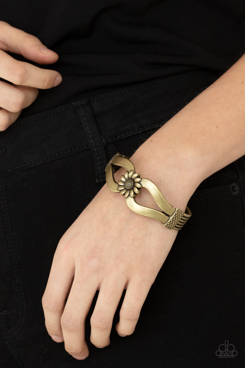 Antiqued brass ribbons loop out from a decorative brass sunflower that attaches to a ribbed brass frame, creating a cuff-like bangle 