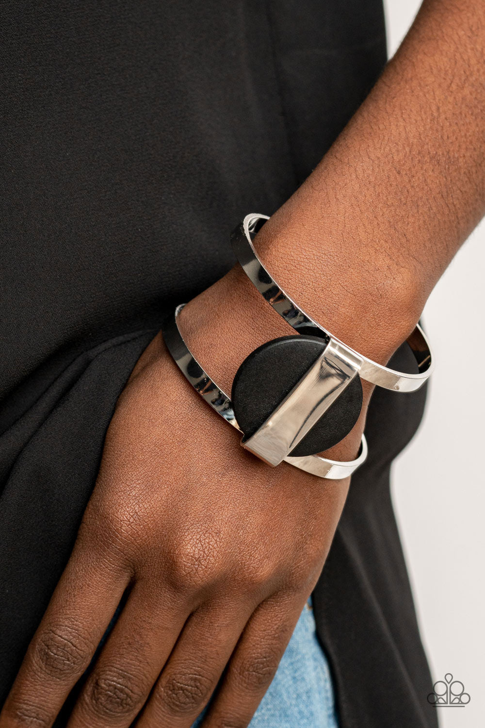 shiny silver frame wraps around an earthy black wooden disc, creating an abstract centerpiece atop a bold silver cuff