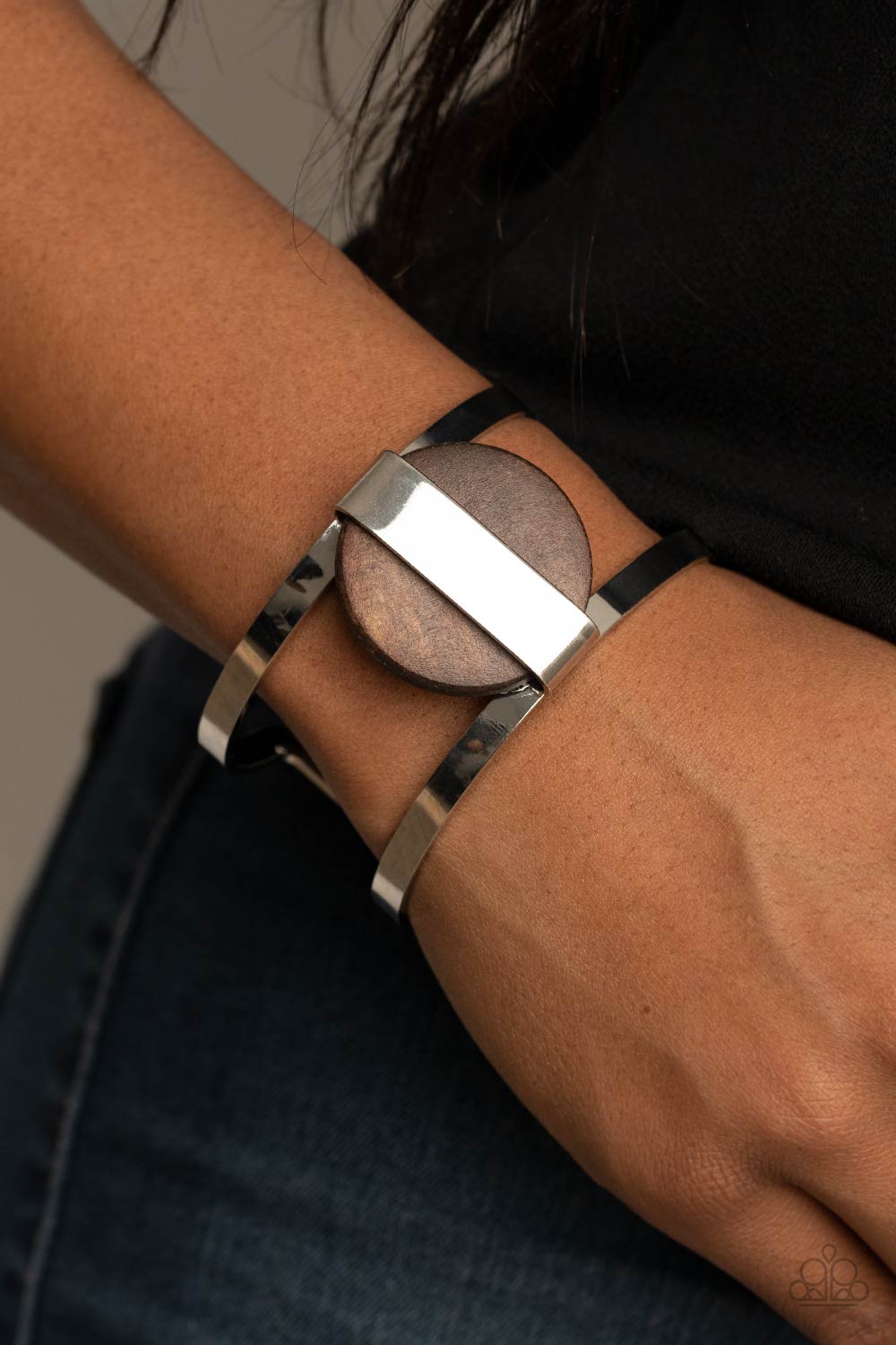 A shiny silver frame wraps around an earthy wooden disc, creating an abstract centerpiece atop a bold silver cuff