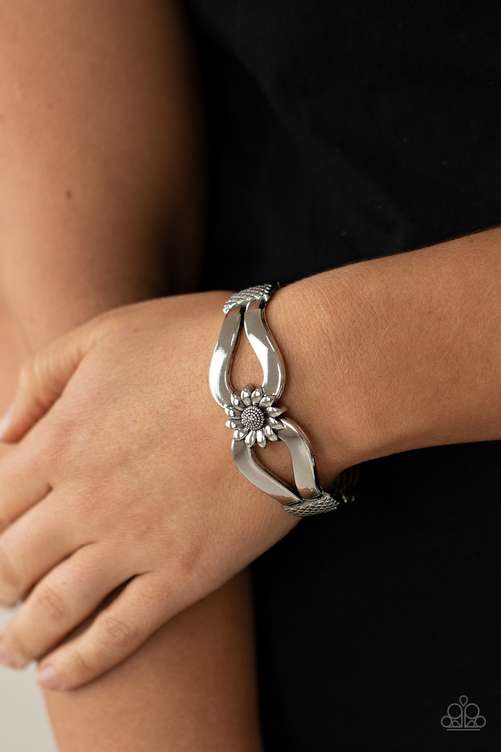 Antiqued silver ribbons loop out from a decorative silver sunflower that attaches to a ribbed silver frame, creating a cuff-like bangle around the wrist