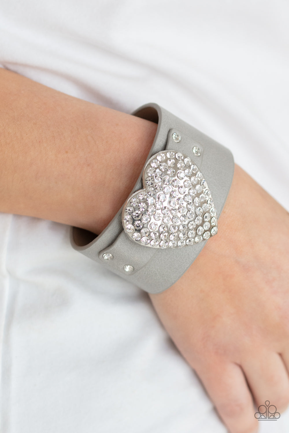 white rhinestones, an oversized silver heart frame is studded in place across the front of a gray leather band