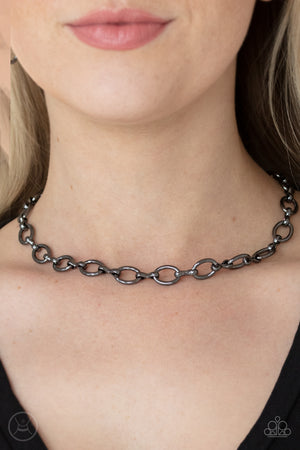 A collection of oversized gunmetal ovals and glistening gunmetal fittings interlock around the neck, creating an intense industrial look