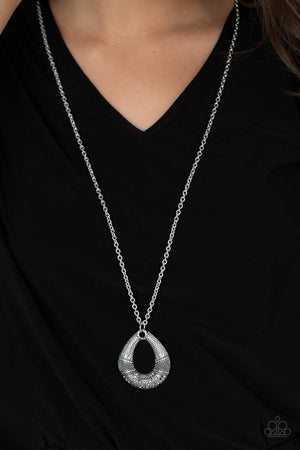 Studded and embossed in bands of texture, the bottom of a hammered silver teardrop is encrusted in smoky hematite rhinestones, creating a glitzy pendant at the bottom of a lengthened silver chain