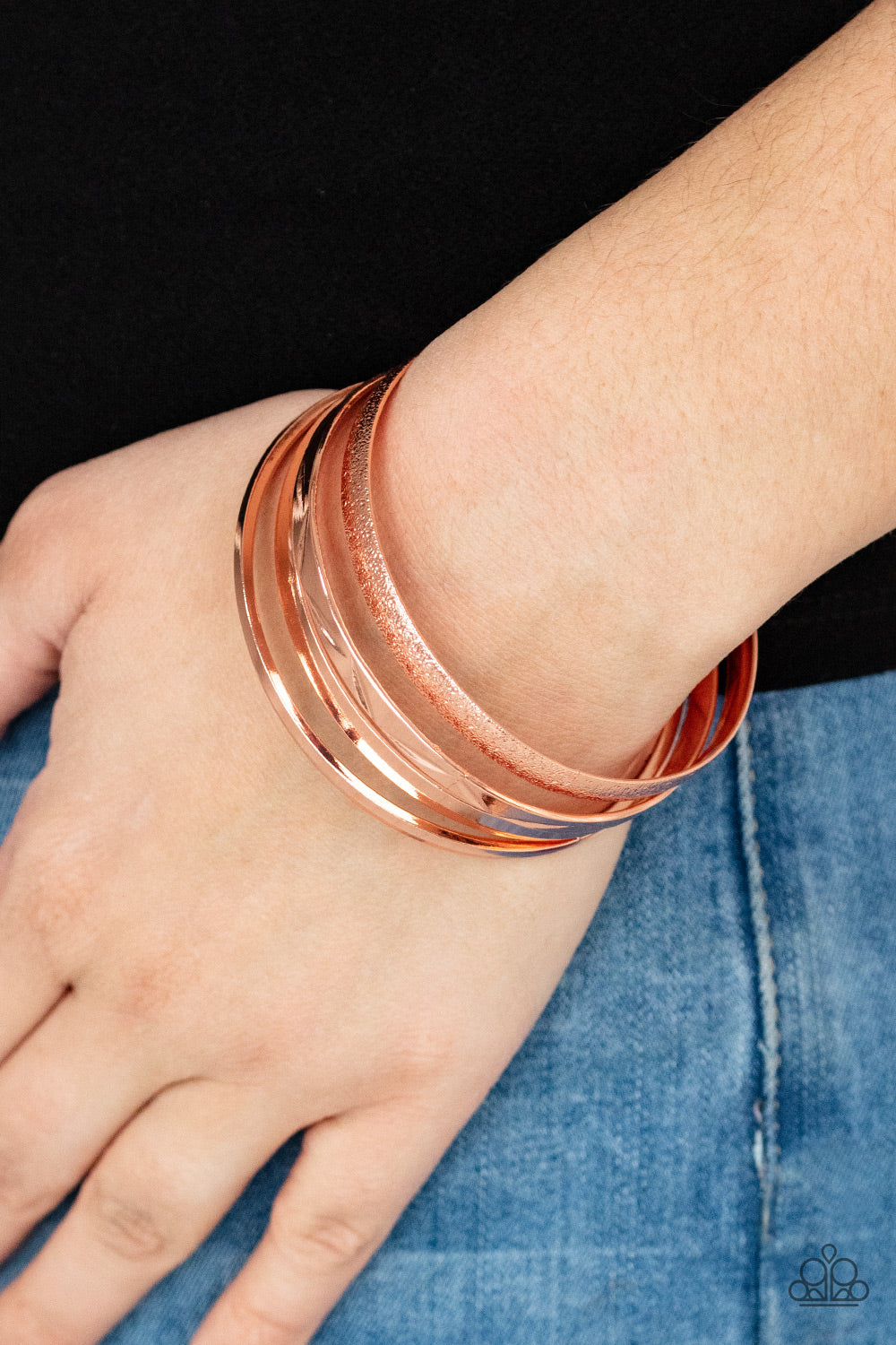 Varying in hammered, textured, and high sheen finishes, a mismatched collection of shiny copper bangles 