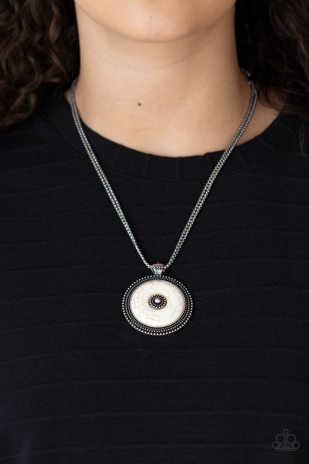  smooth white stone disc is pressed into a textured silver frame radiating with rings of silver studs