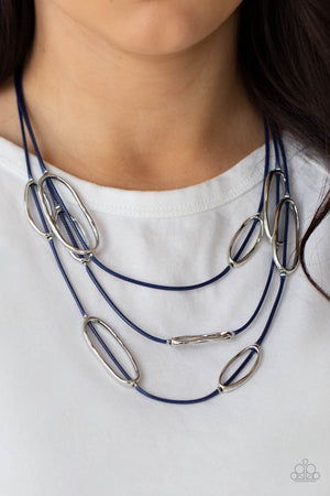 An asymmetrical collection of hammered silver ovals are fitted in place along three rows of shiny blue cords