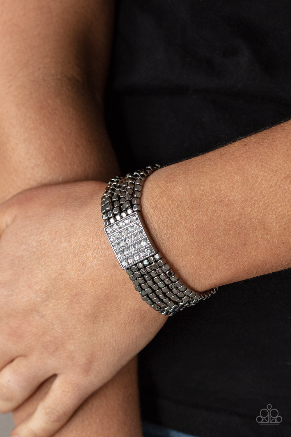 Held in place by a square centerpiece encrusted in row after row of dazzling white rhinestones, a dainty collection of gunmetal cube beads are threaded along stretchy bands around the wrist