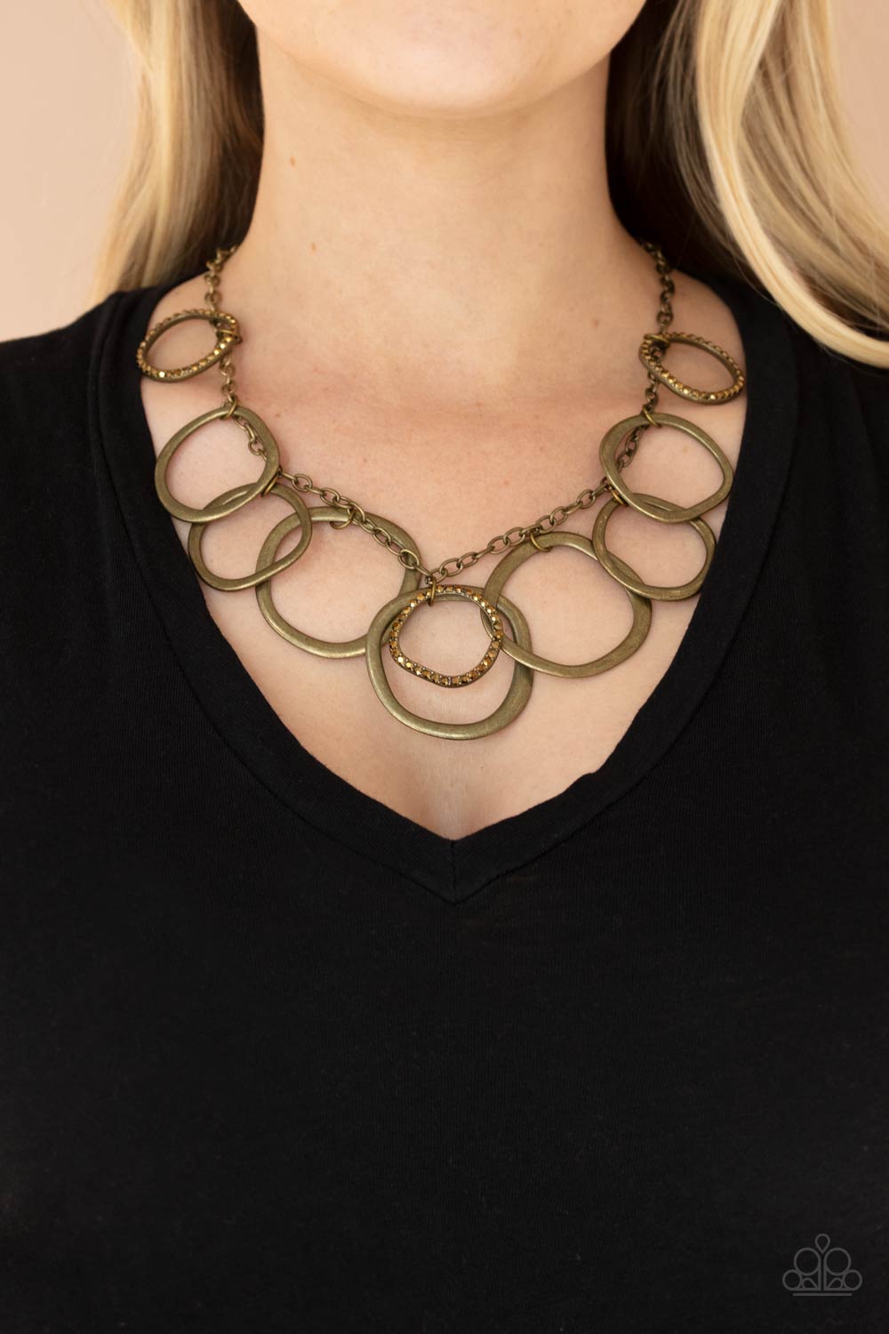 Oversized asymmetrical brass rings swing from the bottom of a rustic brass chain.