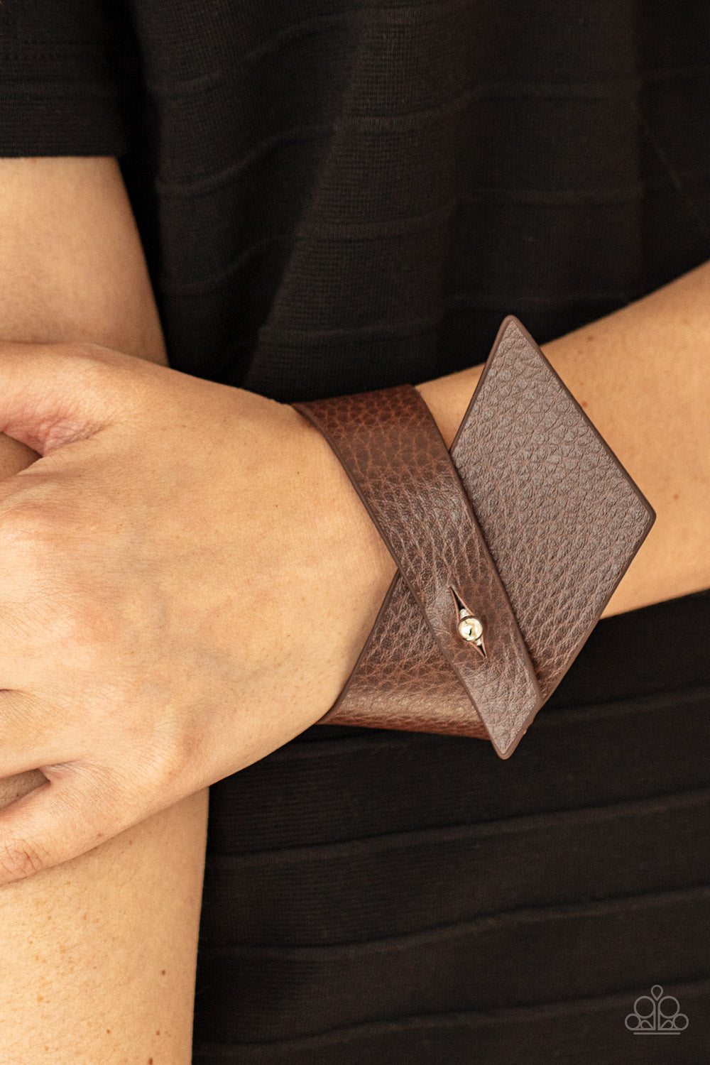 A triangular piece of brown leather delicately wraps around the wrist, creating an edgy asymmetrical centerpiece around the wrist