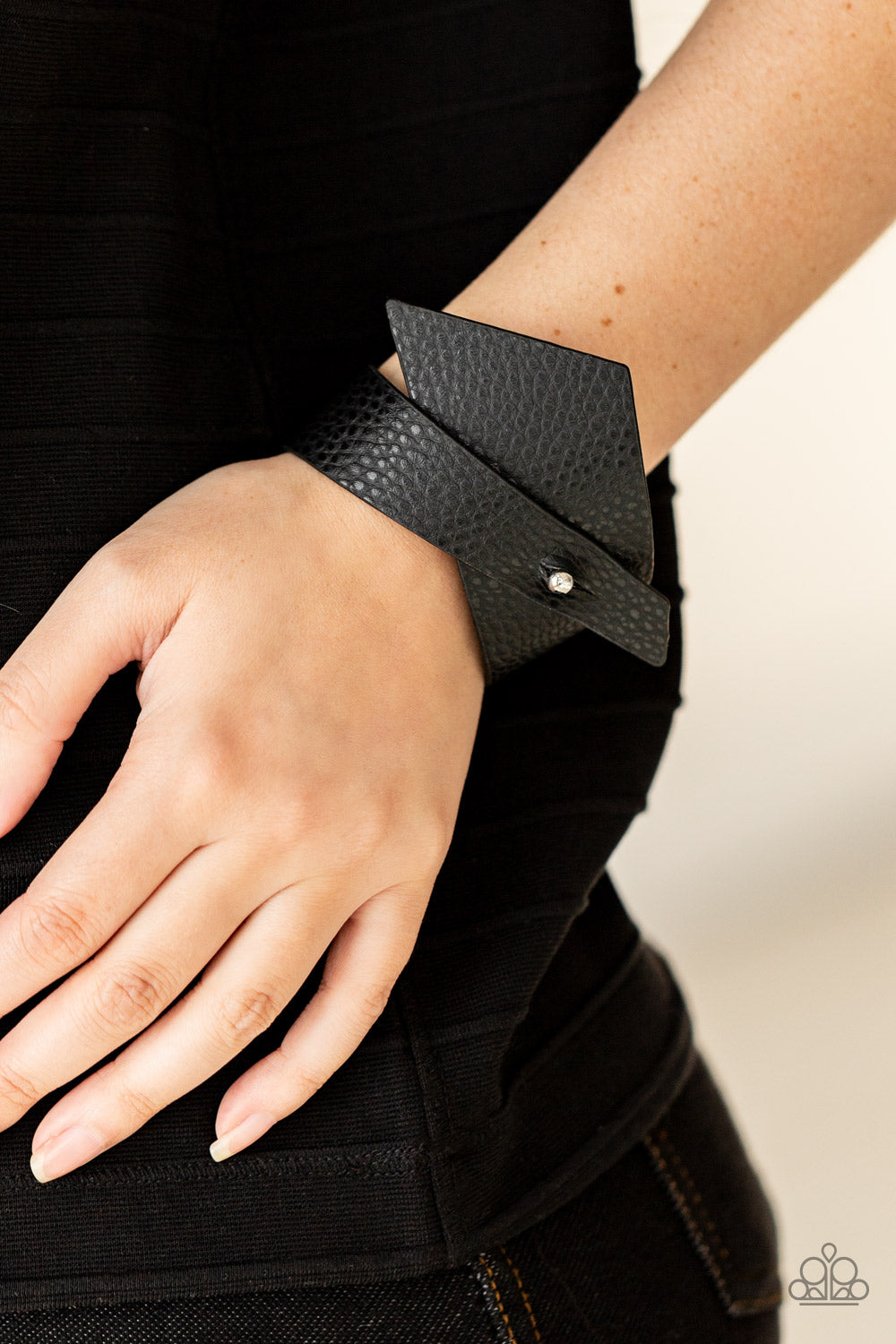 triangular piece of black leather delicately wraps around the wrist, creating an edgy asymmetrical 