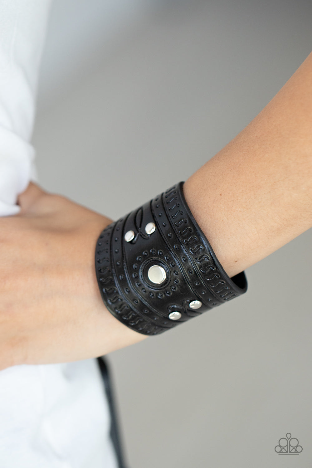 Dotted in shiny silver studs, a triangular piece of black leather is stamped in indigenous inspired patterns for an urban flair.