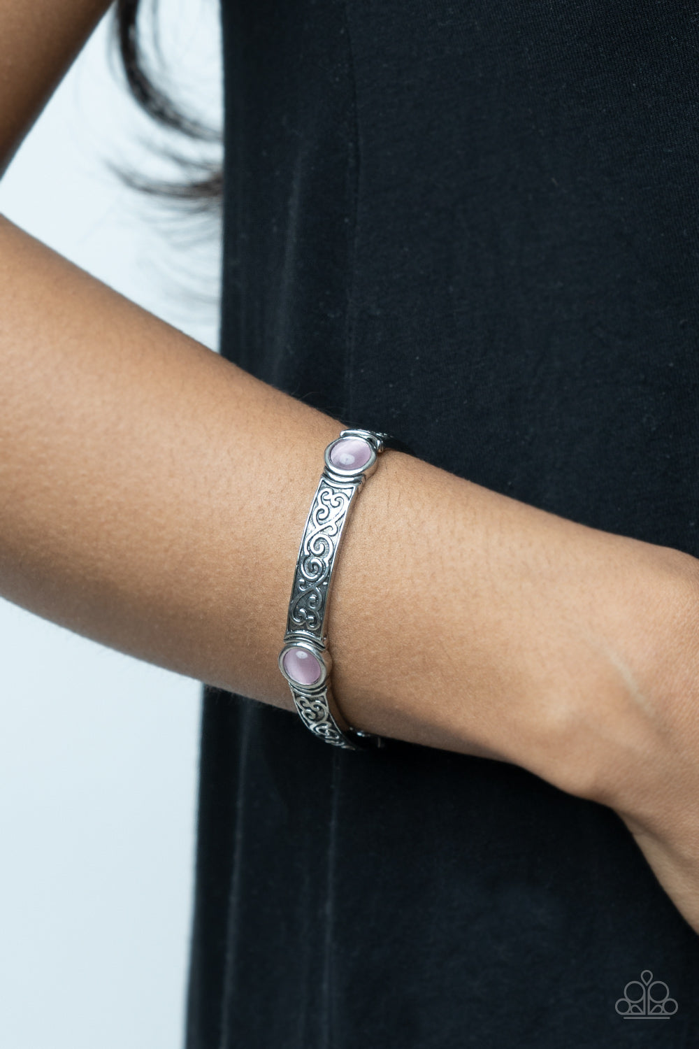 A pink cat's eye stone is pressed into a round frame at the end of a silver bar. 