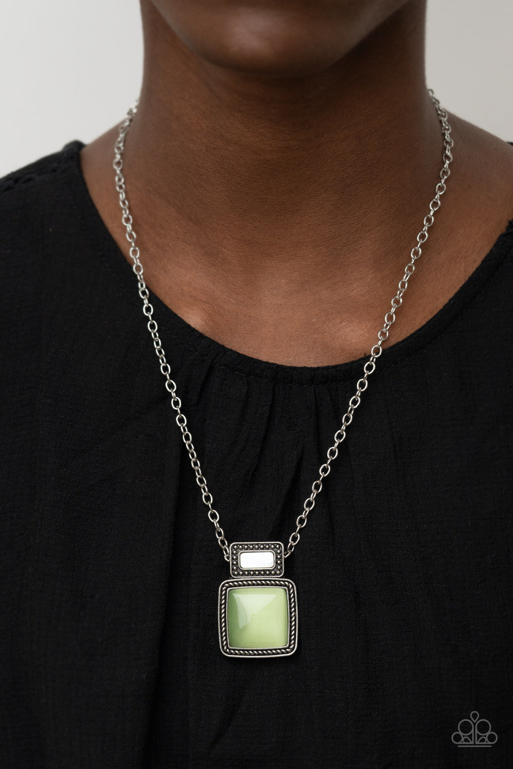 shell-like accent is pressed into the center of a studded silver frame that sits atop a silver rope-like frame that is dotted with a square Green Ash cat's eye stone