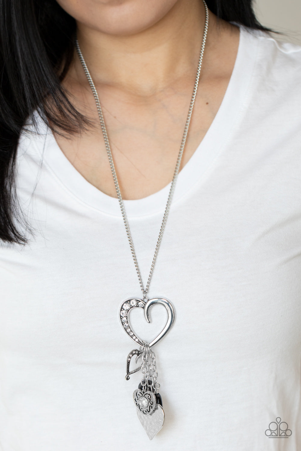 flirtatiously mismatched collection of black beads and ornate silver heart charms swing from the bottom of an oversized silver heart pendant 