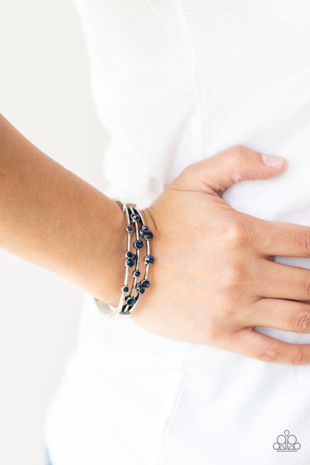 A smattering of glittery blue rhinestones adorn three silver bars that coalesce into a versatile silver cuff-like bangle around the wrist.