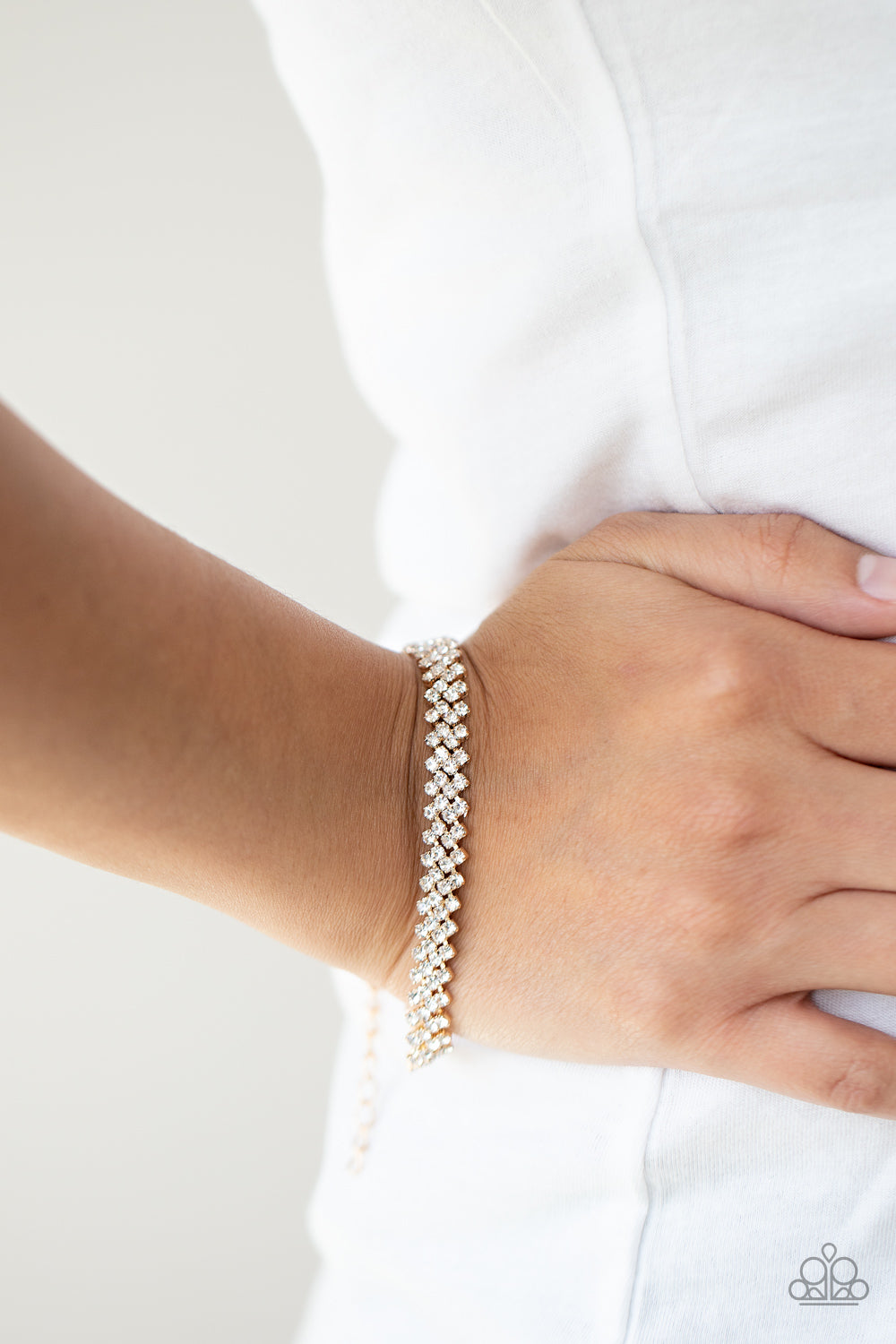 Featuring sleek gold fittings, dainty rows of glassy white rhinestones delicately slant across the wrist, coalescing into a timeless centerpiece