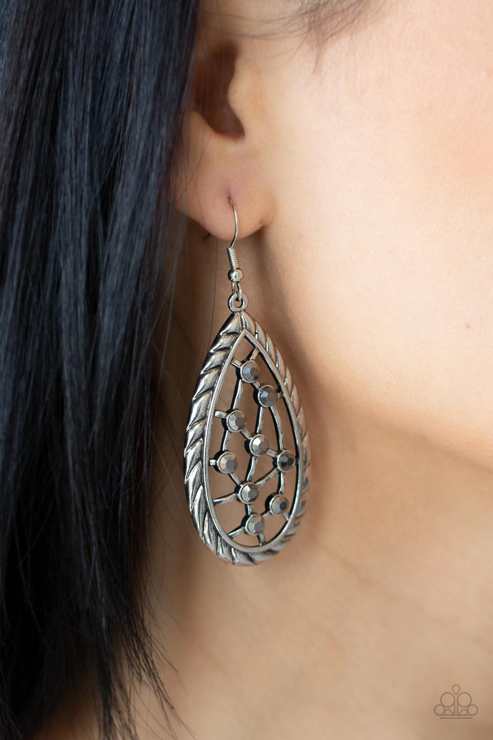 A gritty collection of dainty hematite rhinestones adorn hammered silver bars streaking across the airy center of an antiqued textured teardrop