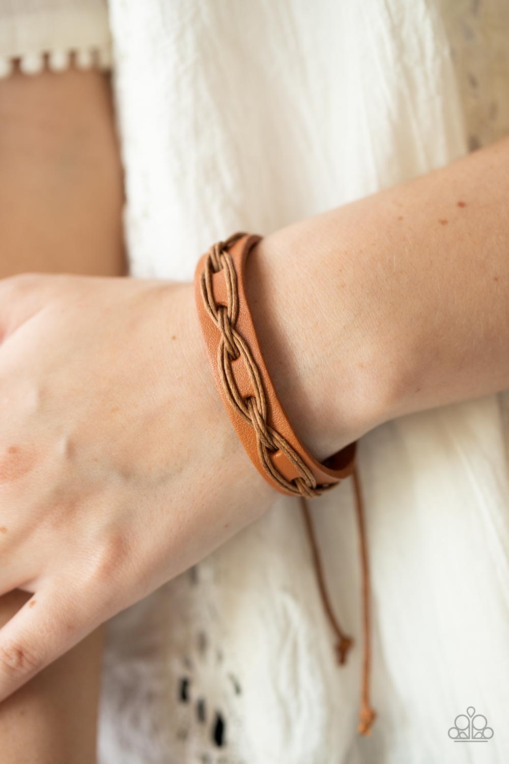 Brown cording is interwoven across the top of a light brown leather band creating an edgy crisscrossed texture around the wrist