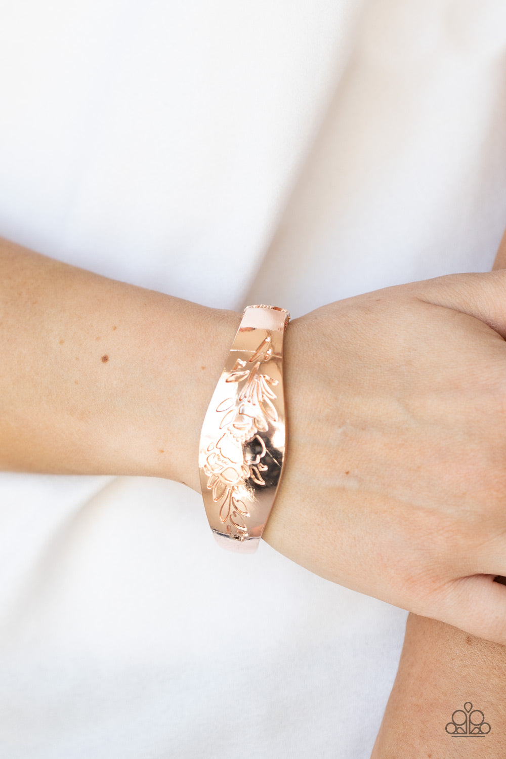 The front of a thick rose gold bangle-like bracelet is stamped in a leafy floral pattern, creating a whimsy centerpiece around the wrist.