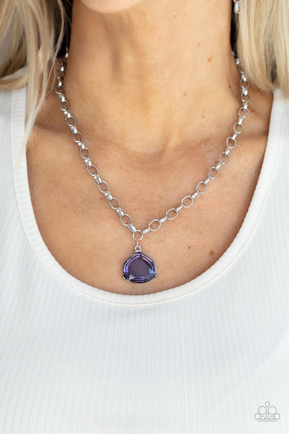 An oversized glassy purple gem is pressed into a pronged silver fitting at the bottom of a chunky silver chain, creating a dramatic pendant below the collar.