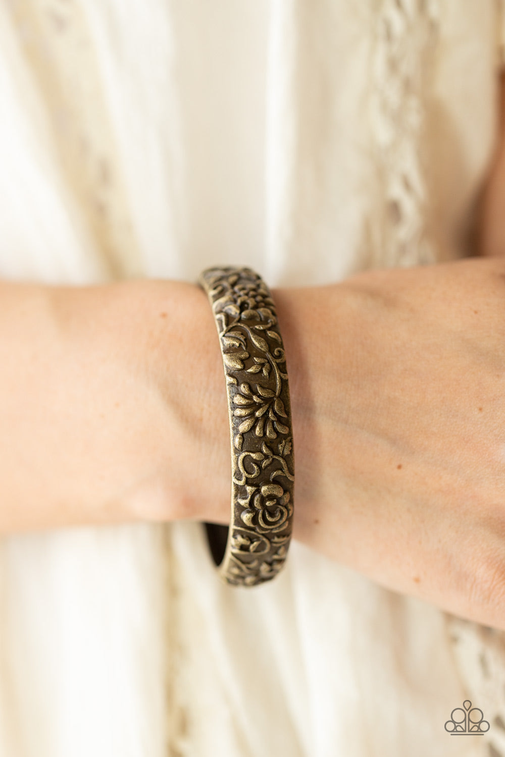 An antiqued brass bangle is delicately embossed in rustic floral patterns, creating a vintage inspired look around the wrist.