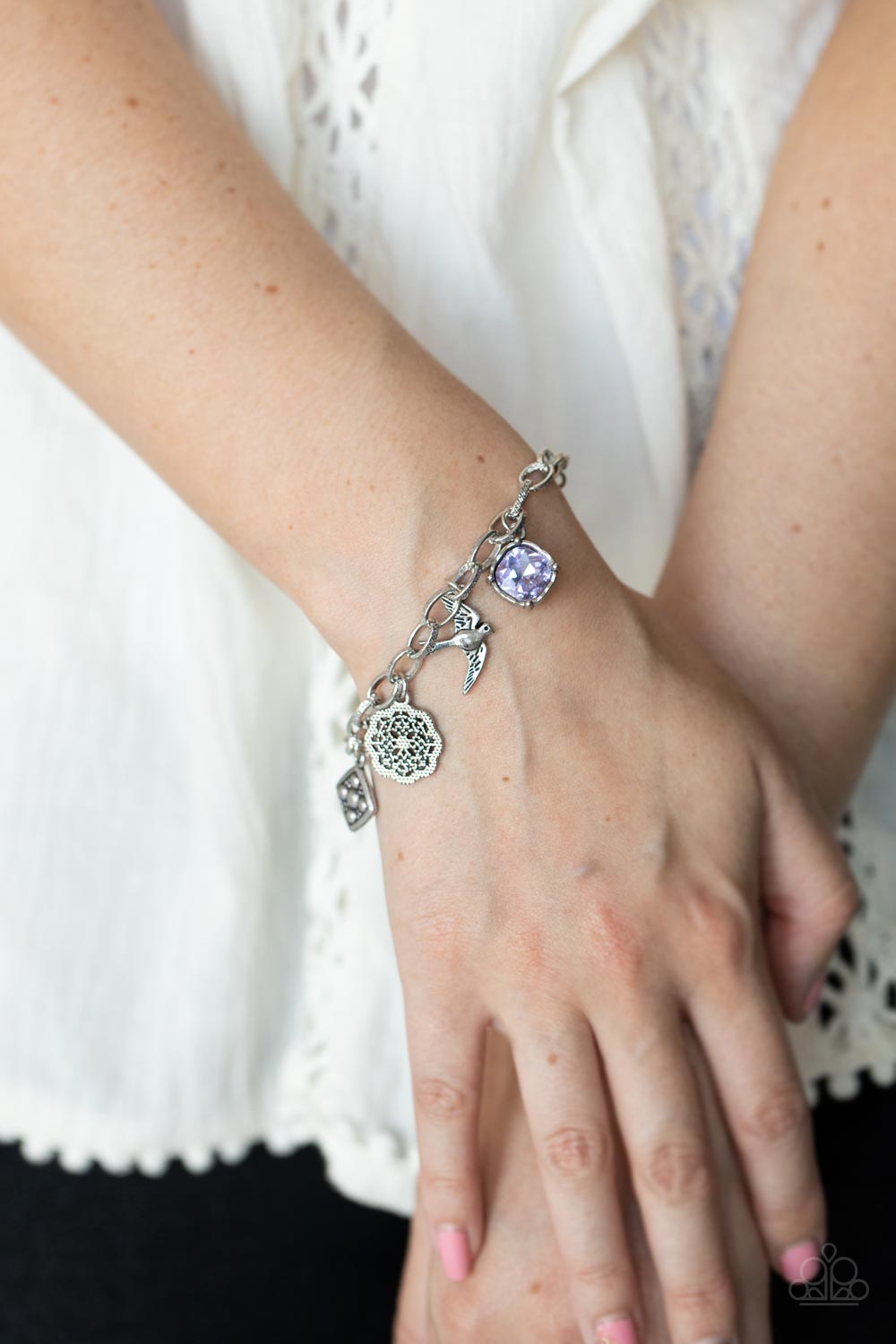 Sparkling purple gems, a floral medallion, a bird in flight, and a fluttering feather dangle from a delicate silver chain