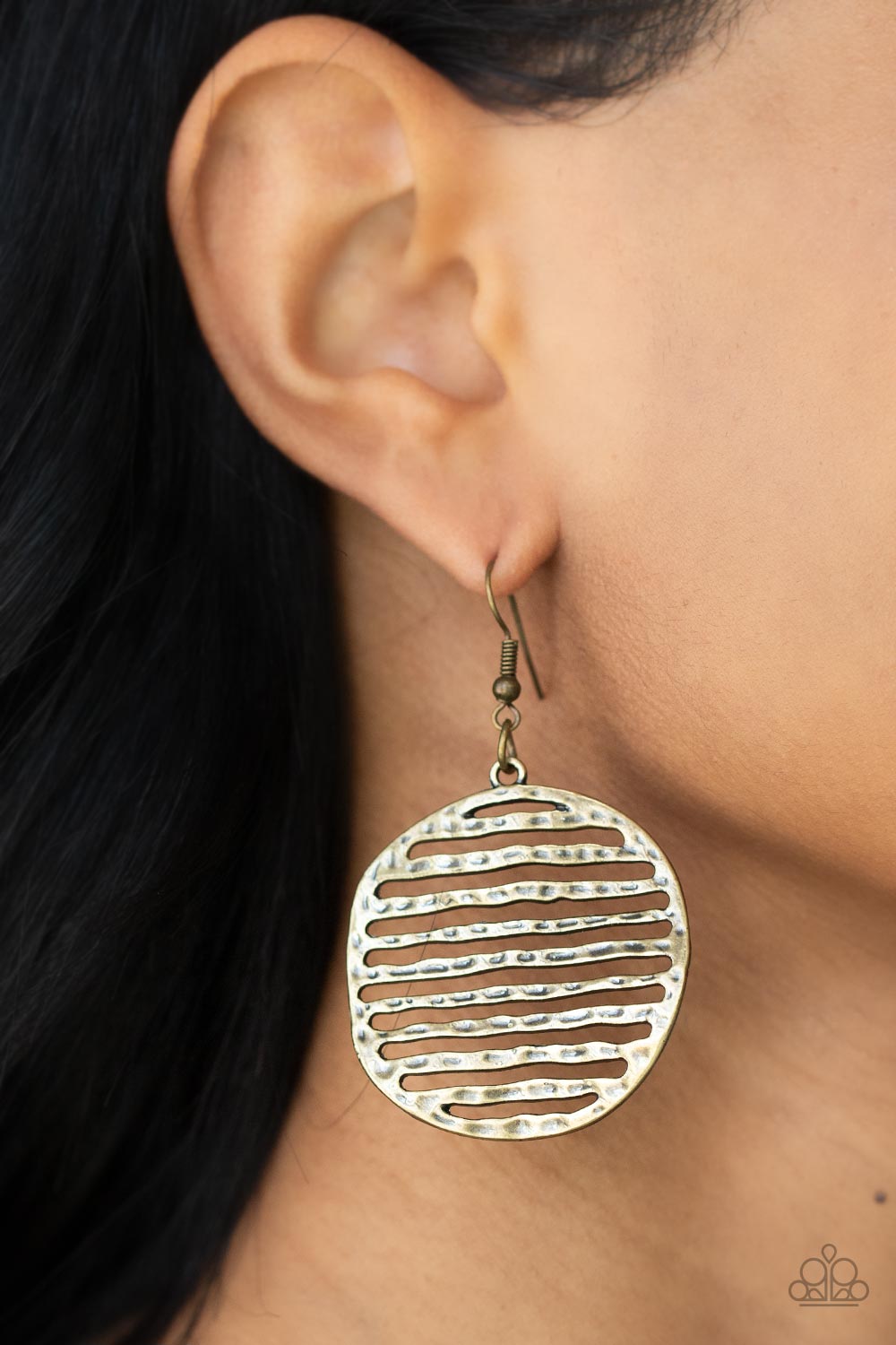 Brushed in an antiqued brass finish, lightly hammered bars stack inside an airy circular frame, creating a wavy rustic lure.