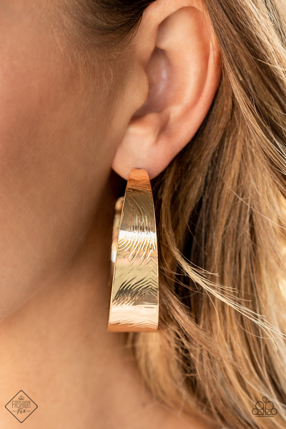 Embossed in whirling geometric details, a thick gold hoop boldly curls around the ear for a curvaceous look.