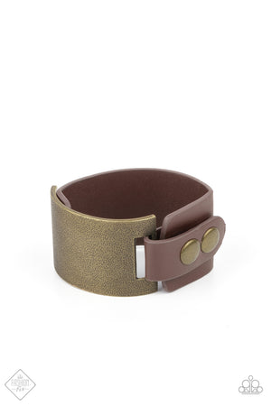 A curved brass panel, coated in antiqued texture, attaches to a wide brown leather band with brass snaps