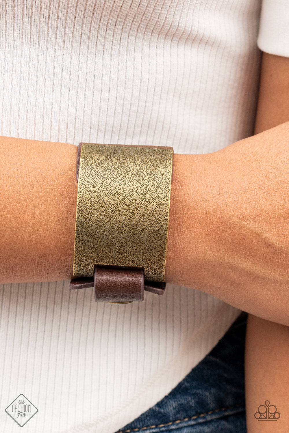 A curved brass panel, coated in antiqued texture, attaches to a wide brown leather band with brass snaps