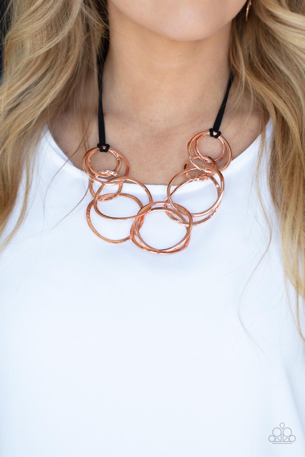 Black suede cords knot around a mismatched assortment of hammered shiny copper rings that interlock below the collar,