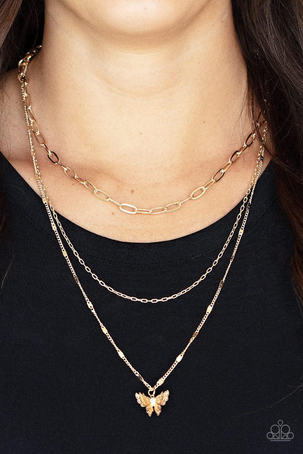Dotted with a dainty white rhinestone, a decoratively layered gold butterfly swings from the bottom of a display of mismatched gold chains