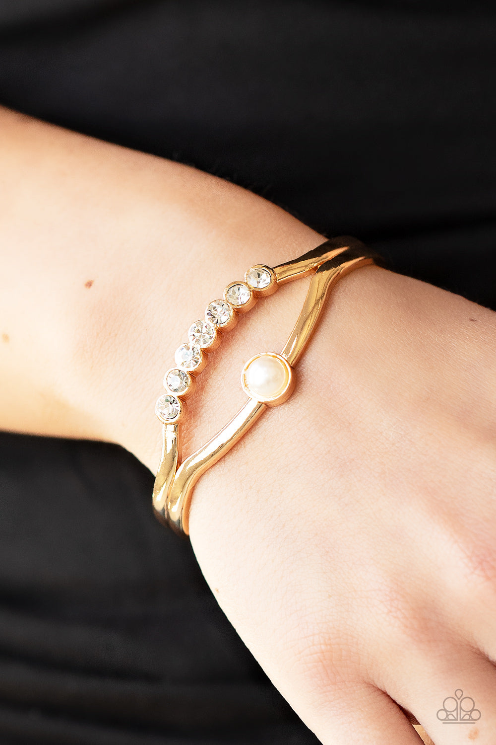 A row of glassy white rhinestones and a solitaire white pearl adorn the layered center of a classic gold cuff