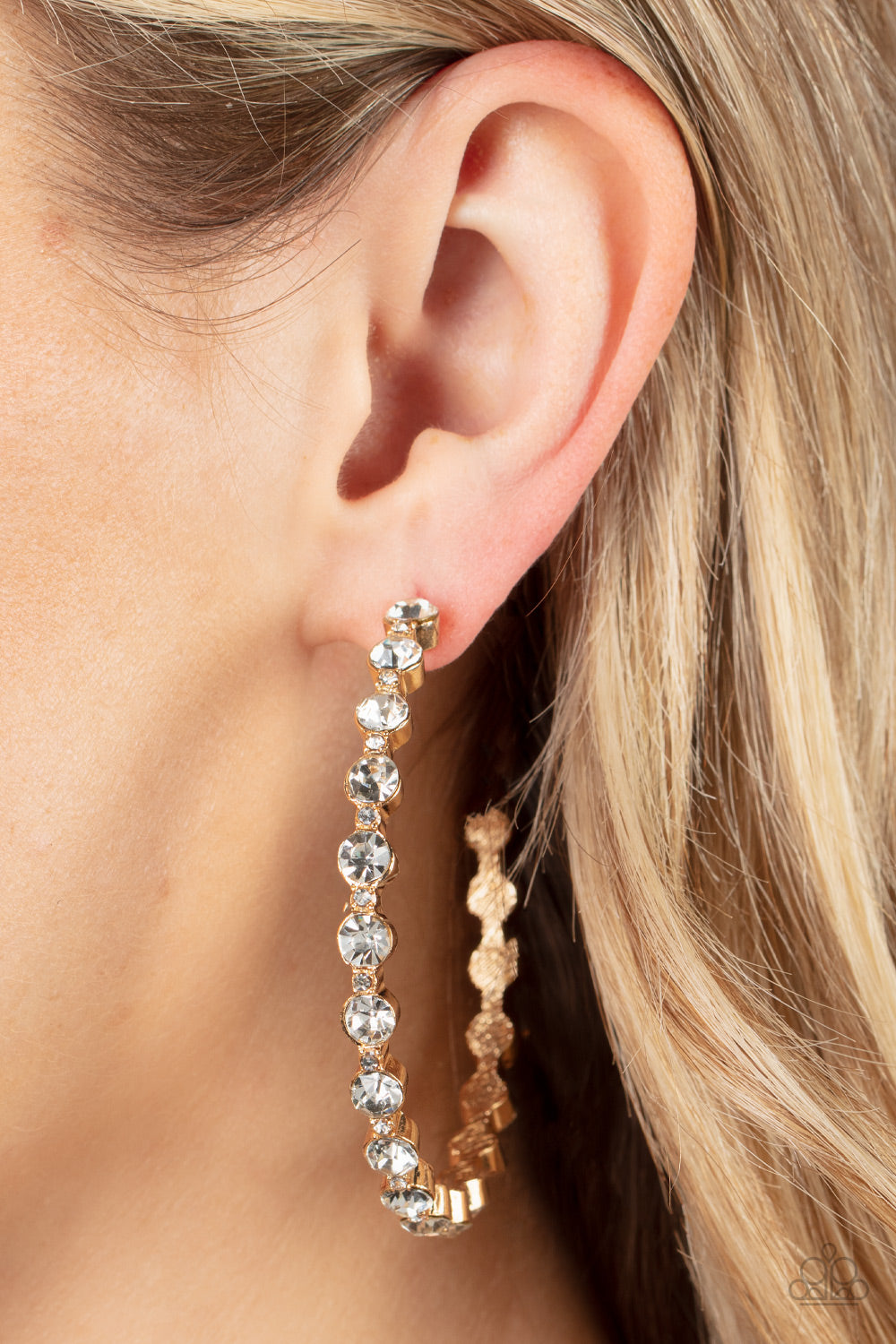 Encased in sleek gold fittings, a glamorous collection of glittery white rhinestones delicately coalesce into an oversized hoop 