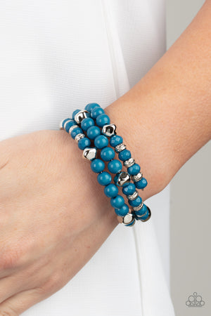 mismatched collection of polished blue and shiny silver beads are threaded along a coiled wire