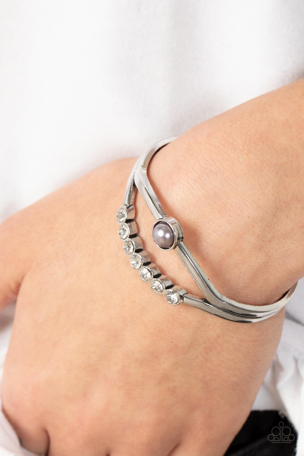 A row of white rhinestones and a solitaire silver pearl adorn the layered center of a classic silver cuff
