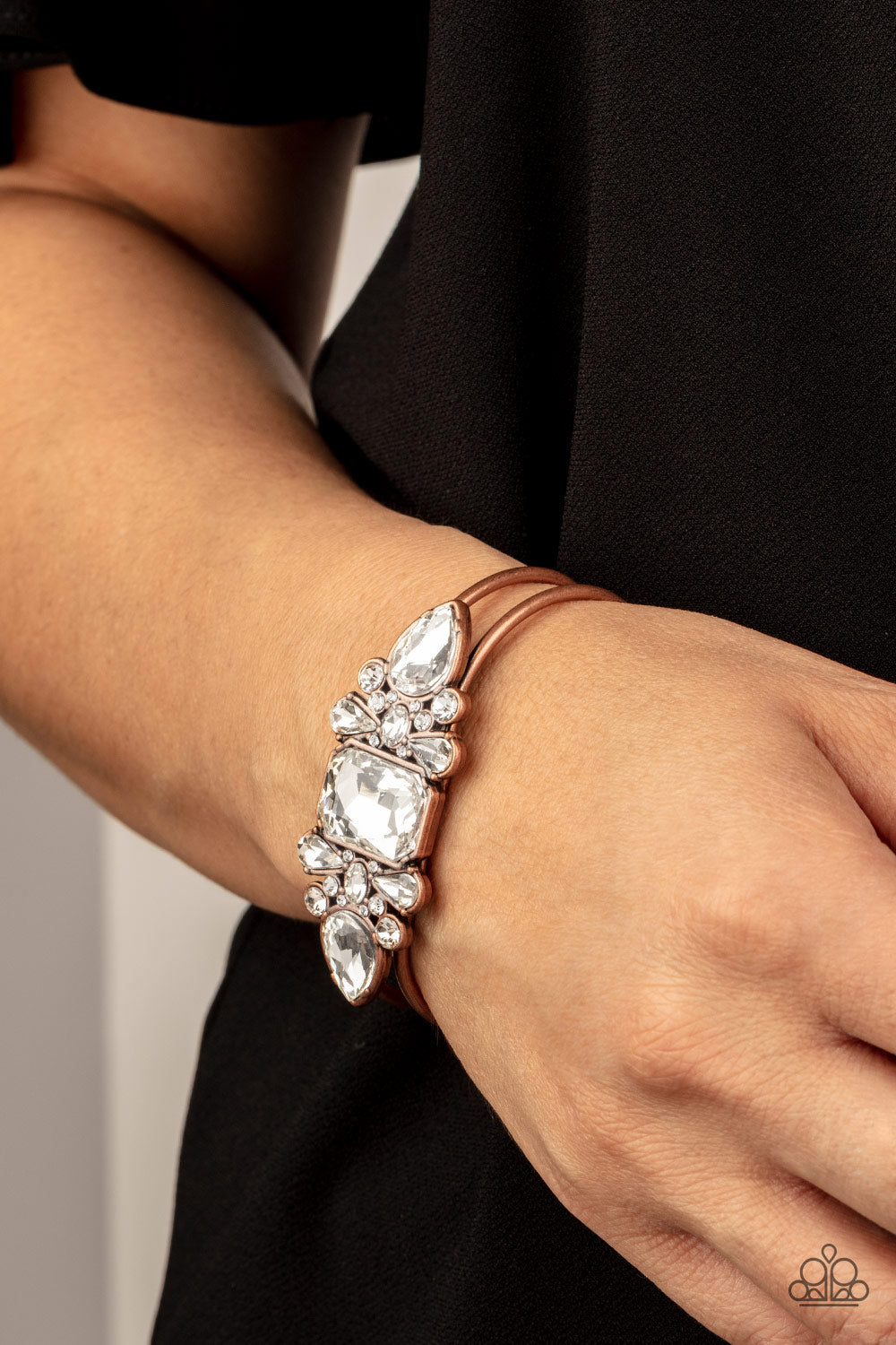 regal teardrop, oval, emerald, and round cuts, an explosion of oversized rhinestones neatly coalesce into a sparkly centerpiece atop an airy copper cuff