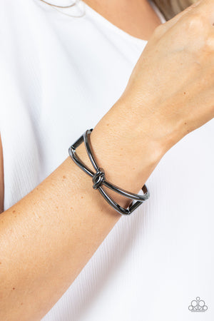 Striking gunmetal bars delicately knot at the top and bottom of the wrist, resulting in an edgy bangle-like bracelet