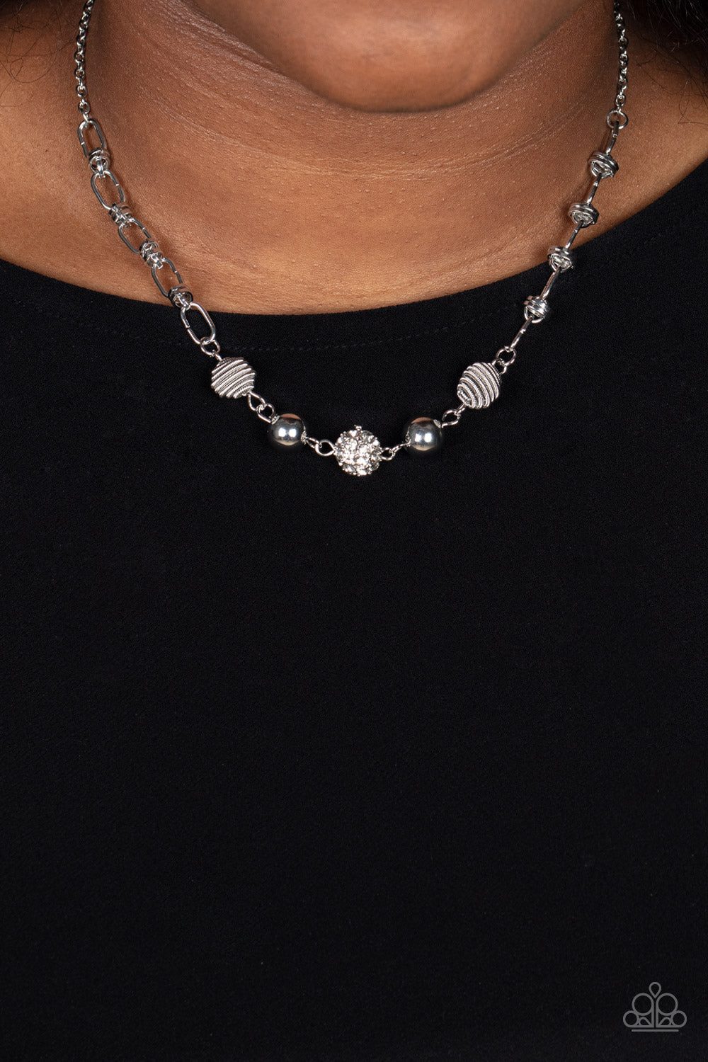 Pairs of silver coiled and smooth silver beads flank a white rhinestone encrusted bead along an oval and silver disc linked chain