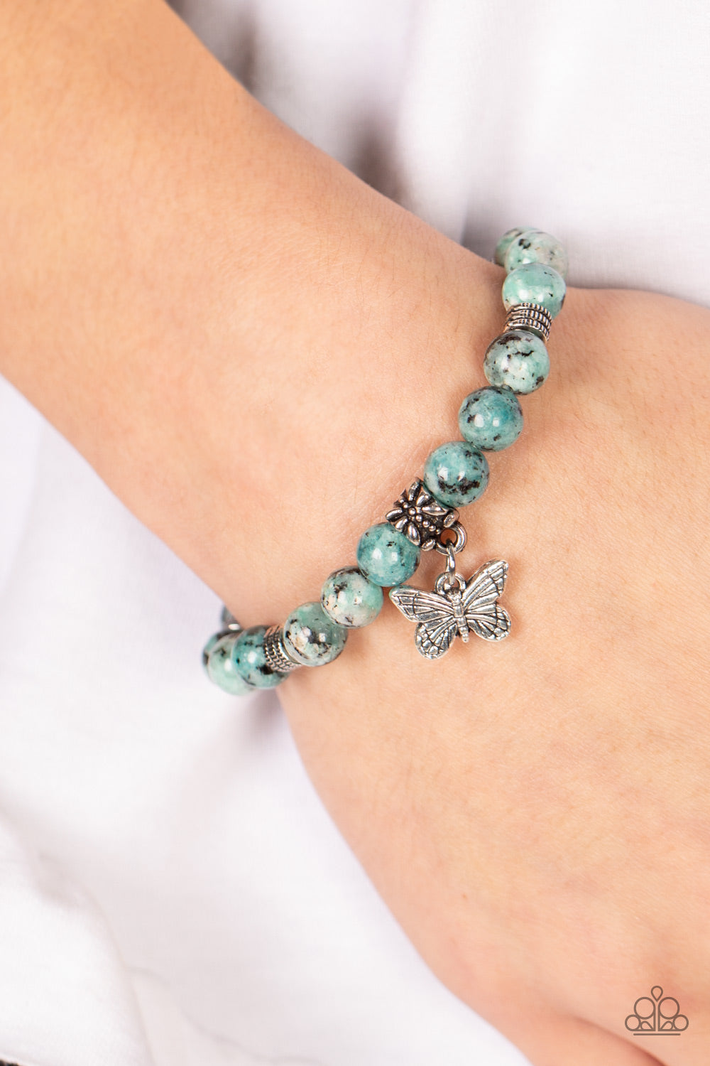 Infused with a silver butterfly charm, textured silver accents and black speckled blue stone beads are threaded along stretchy bands