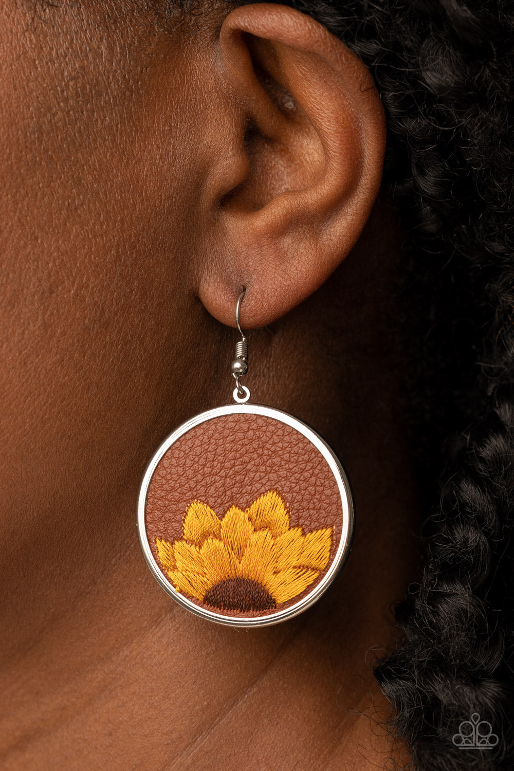 golden yellow and brown threaded sunflower is stitched into the bottom of a brown leather frame that is encased in a sleek silver frame