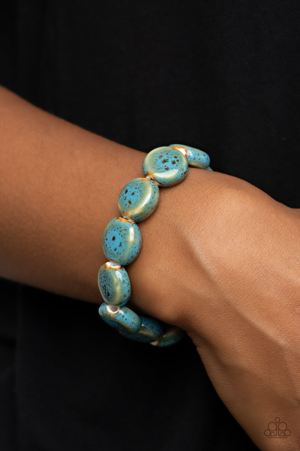 Glazed in a distressed blue finish, an oversized collection of ceramic beads are threaded along a stretchy band