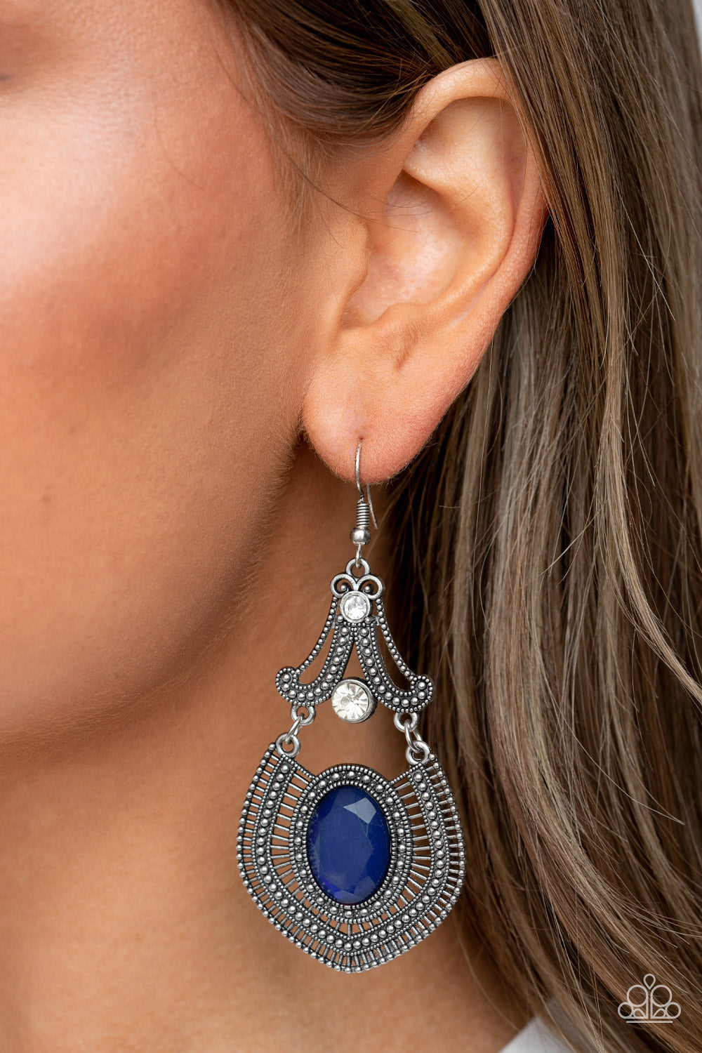 Studded silver detail and dainty silver bars fan out from an oversized blue gem at the bottom of a white rhinestone dotted frame