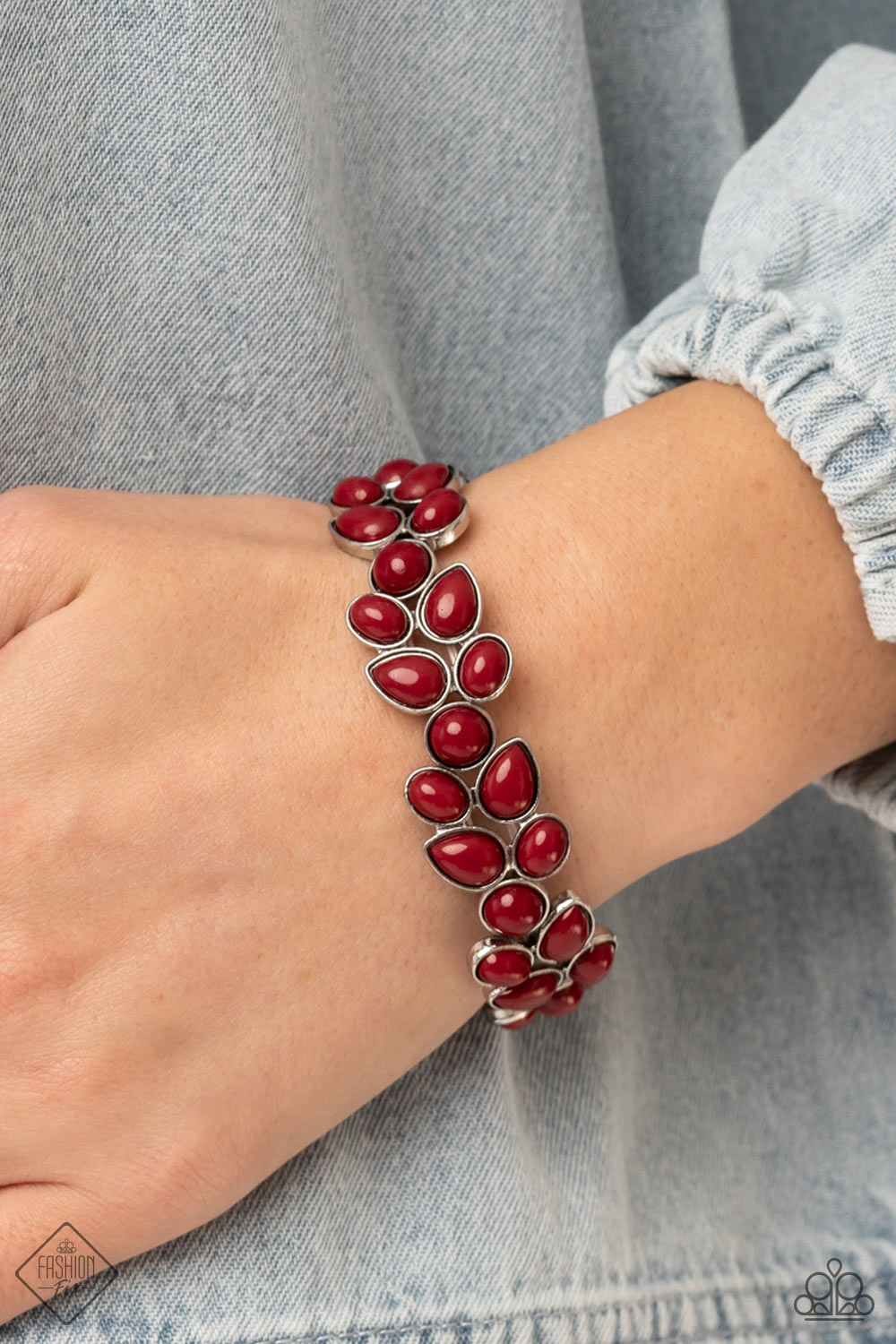 red oval, round, and teardrop beads coalesce into abstract floral-inspired frames. The enchanting frames, threaded along stretchy bands
