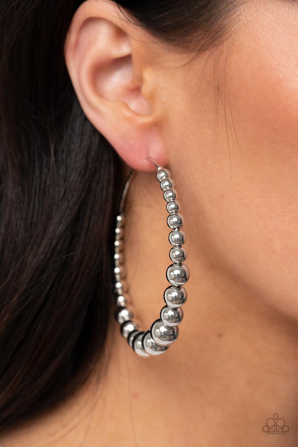 Gradually increasing in size, shiny silver beads are threaded along an oversized silver hoop