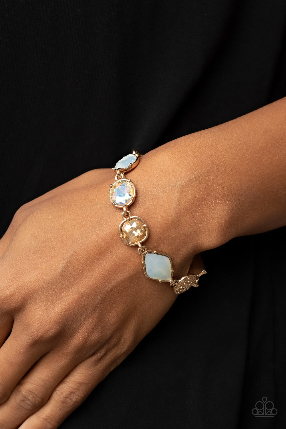 Encased in pronged gold fittings, a mismatched collection of golden, iridescent, and opal rhinestones delicately links with a studded gold frame around the wrist